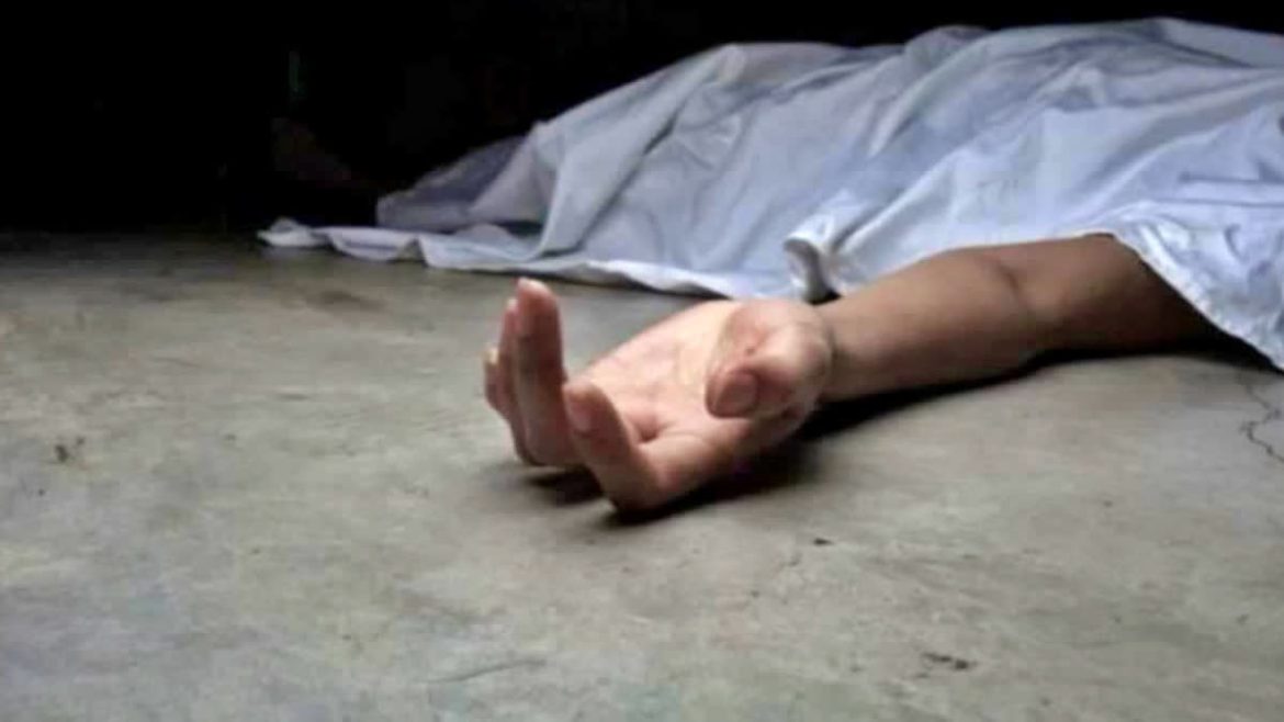 A lifeless hand reaches out from beneath a white sheet, lying on a concrete floor in a dimly lit environment.