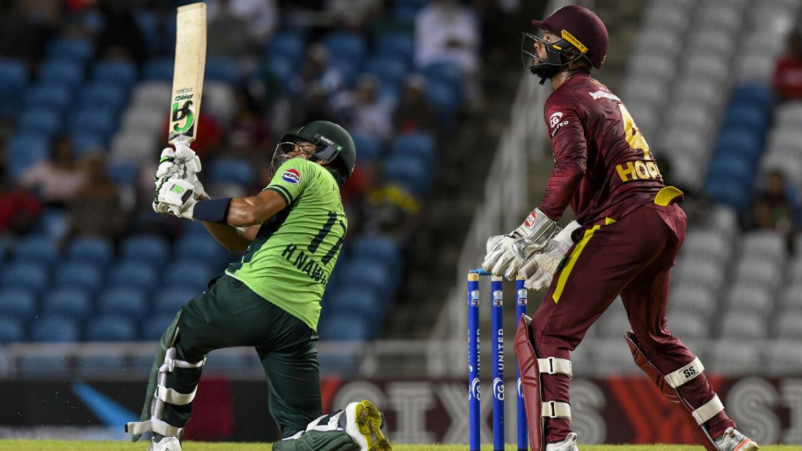 A cricket player in a green uniform swings a bat, while a West Indies player in maroon watches from behind.