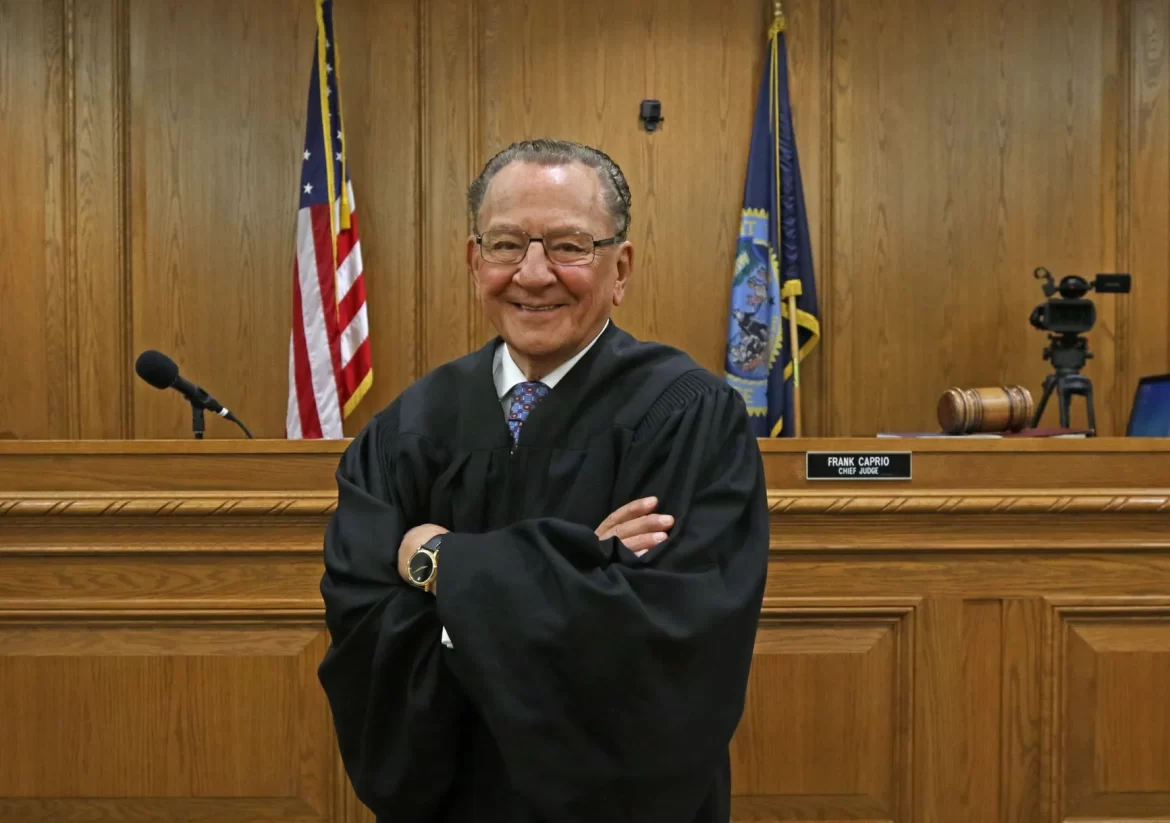 A world kindest judge Frank Caprio in a black robe stands confidently in a courtroom, with American flags and a gavel in the background.