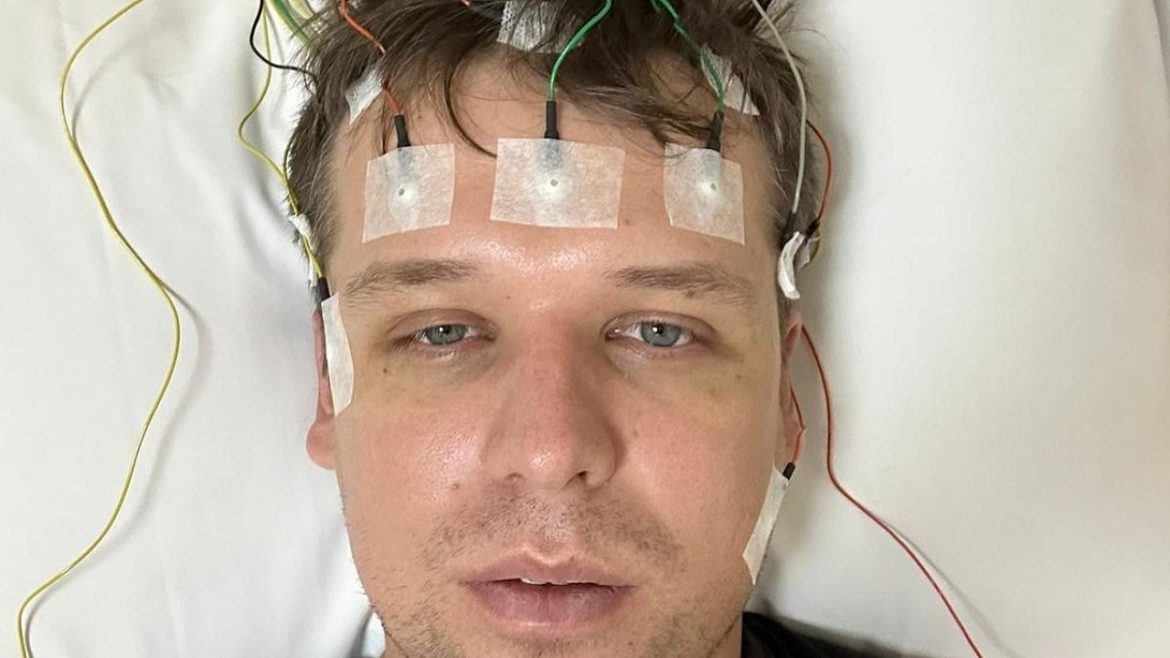 A person lies on a white surface with multiple colorful wires attached to their head, indicating a medical procedure or monitoring.