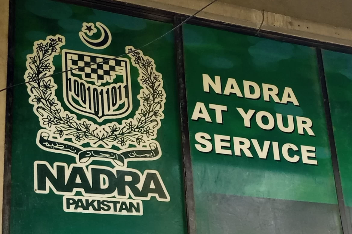 A close-up of a sign displaying "NADRA AT YOUR SERVICE" alongside the NADRA logo and the emblem of Pakistan.