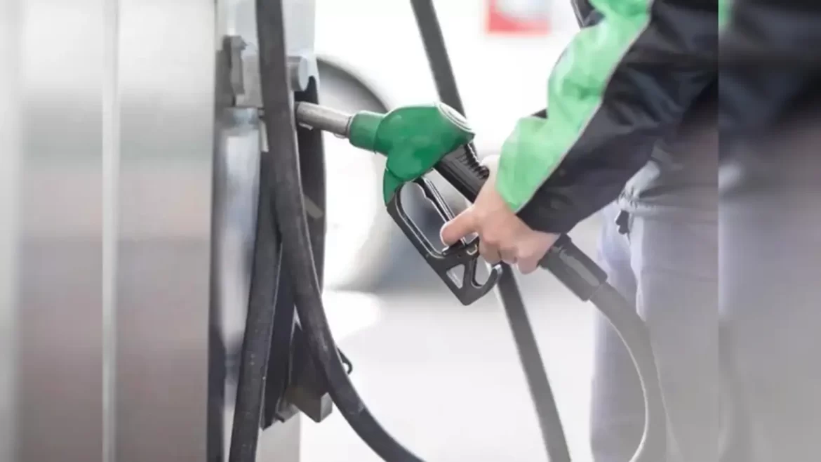 A person in a green jacket holds a green fuel pump nozzle, preparing to refuel a vehicle at a gas station.