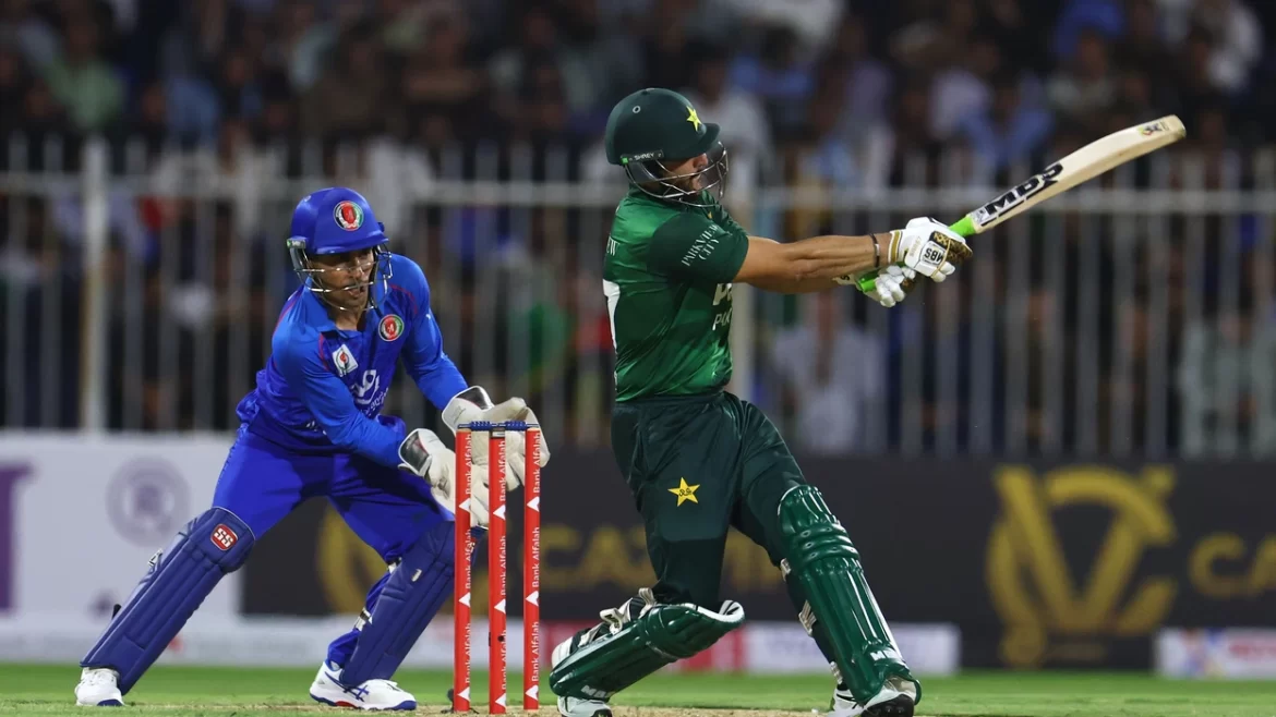 A cricketer in green swings a bat fiercely while another player in blue prepares to catch during an intense match.