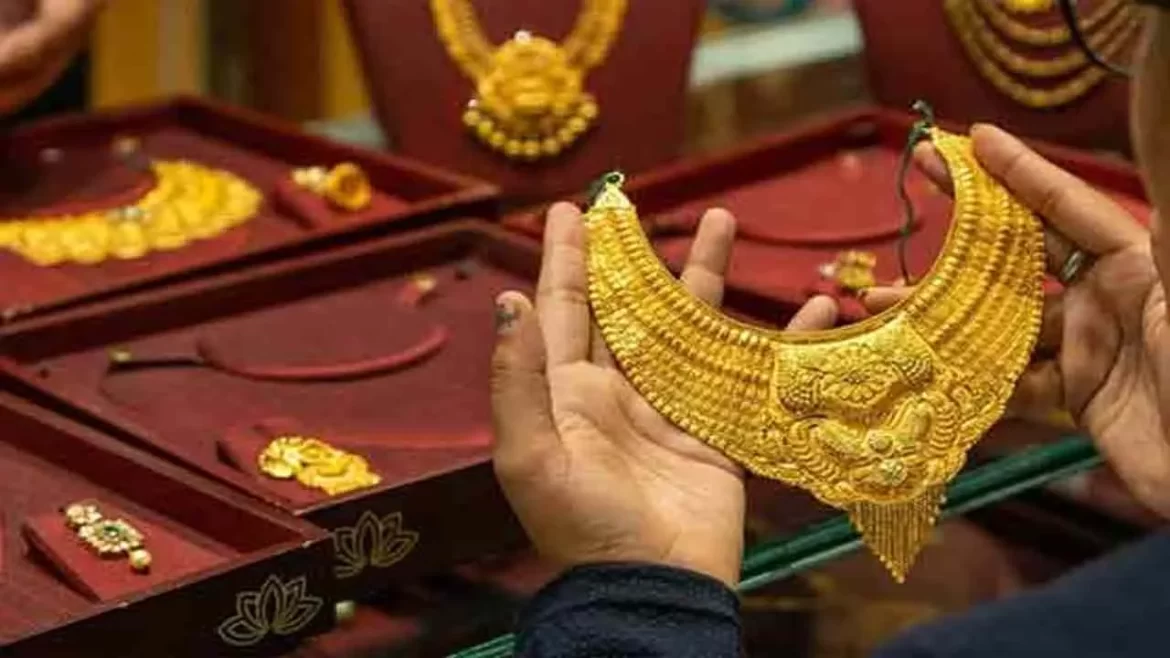 A person examines an ornate gold necklace, surrounded by various pieces of jewelry displayed in a maroon velvet box.