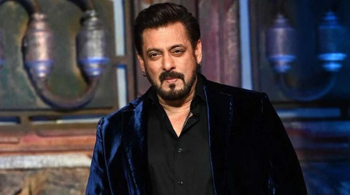 A man in a stylish velvet blazer stands confidently against a textured backdrop with industrial elements, exuding charm and charisma.