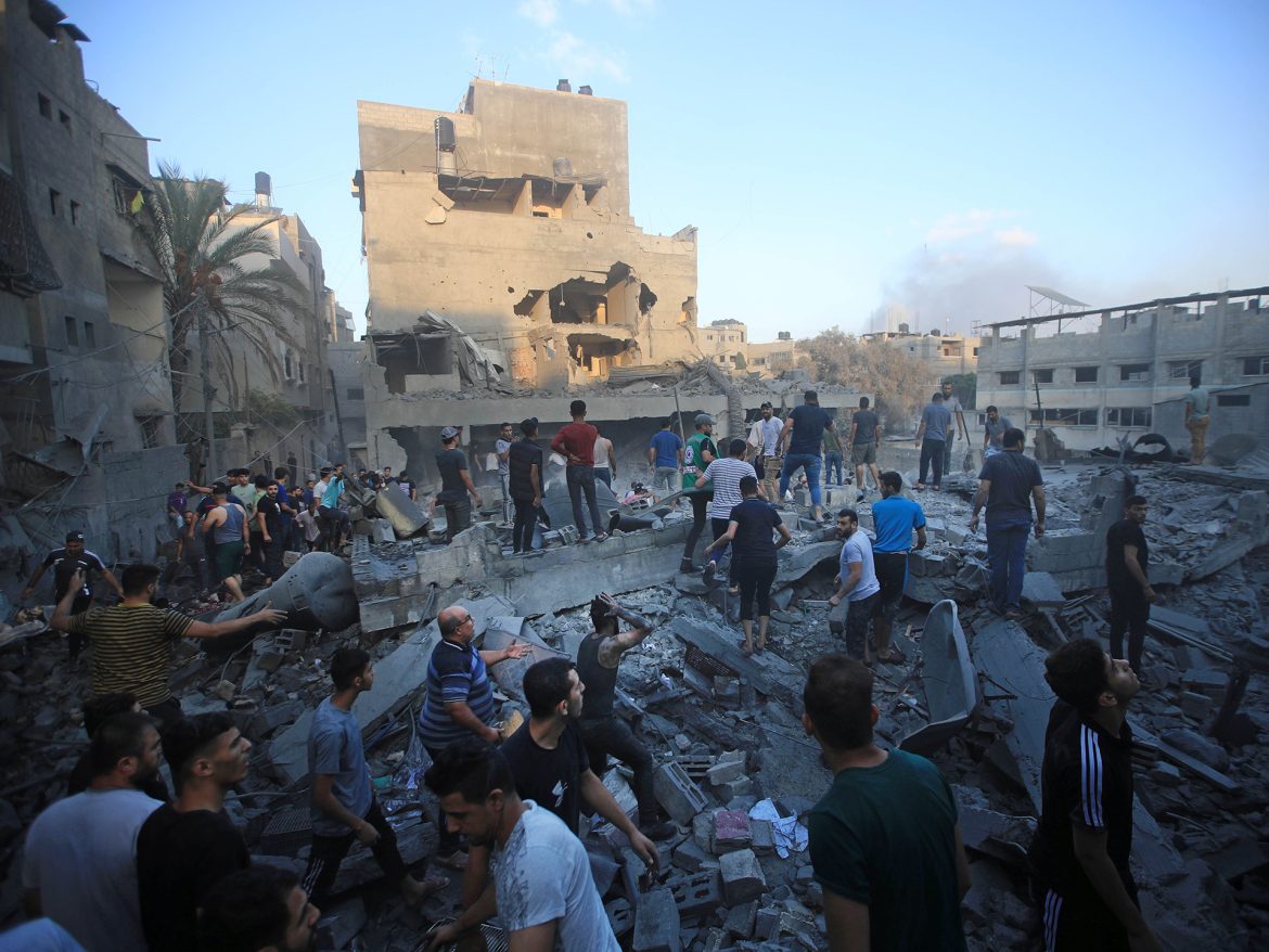 A crowd of people sifts through rubble and debris from destroyed buildings, assessing the damage in a devastated urban area.