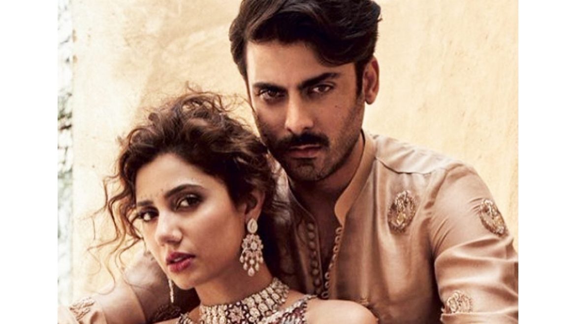 A couple poses closely together, dressed in elegant traditional outfits, against a soft, neutral background.