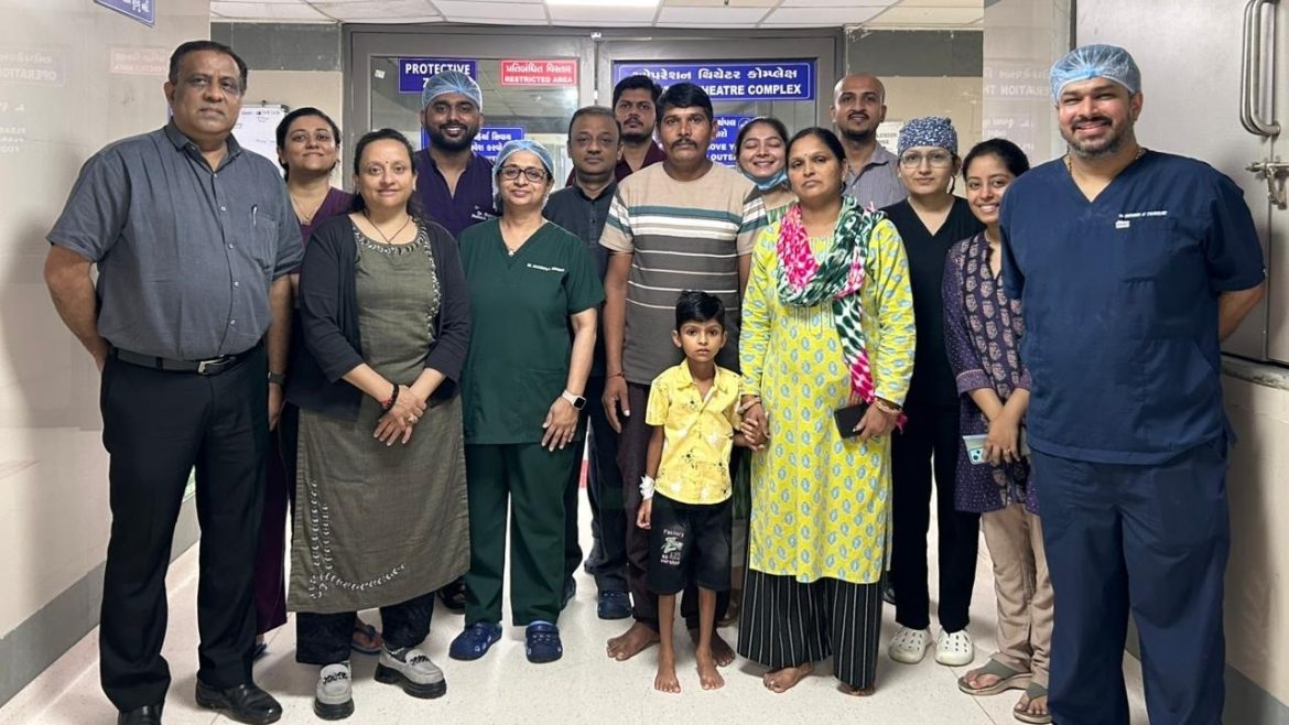A group of diverse individuals, including medical staff and family members, poses together in a hospital corridor.