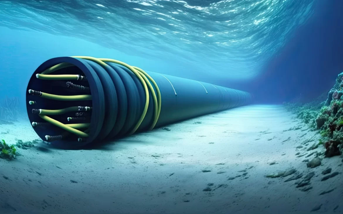 A large, coiled underwater cable lies on the ocean floor, surrounded by sand and coral, beneath gently rippling water.