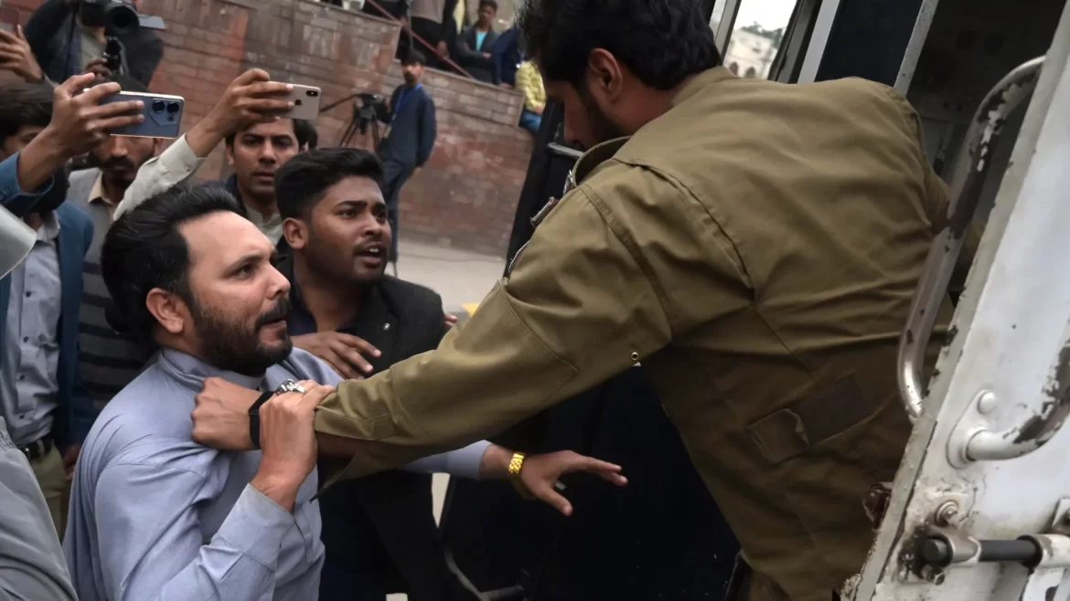 A police officer is apprehending a man as onlookers capture the moment on their smartphones in a crowded urban setting.