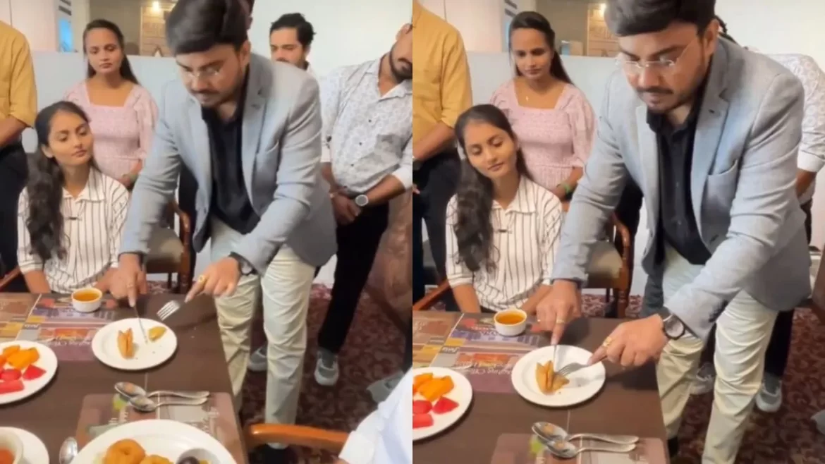 A man in a blazer cuts a dessert while seated diners look on, surrounded by colorful plates of food and a cup of tea.