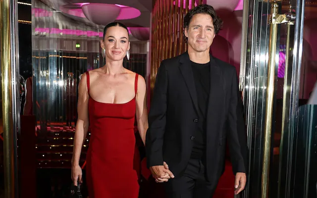 A couple walks hand-in-hand in a stylish venue, the woman in a striking red dress and the man in a sleek black suit.