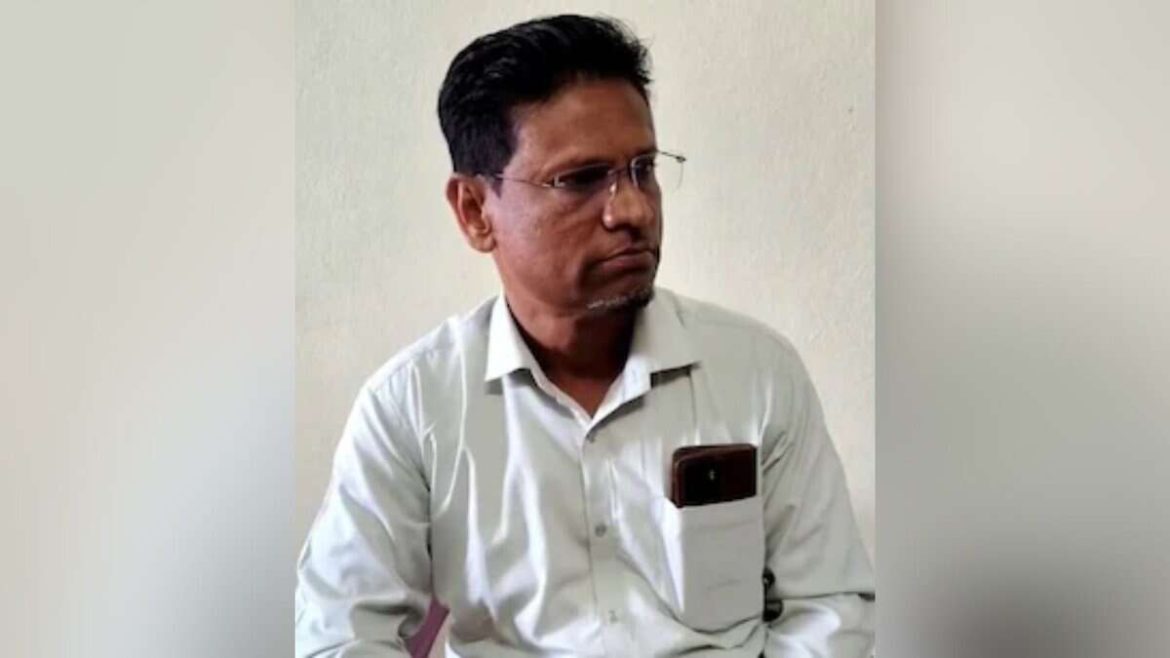 An person in a white shirt sits against a plain background, a smartphone partially visible in their shirt pocket.