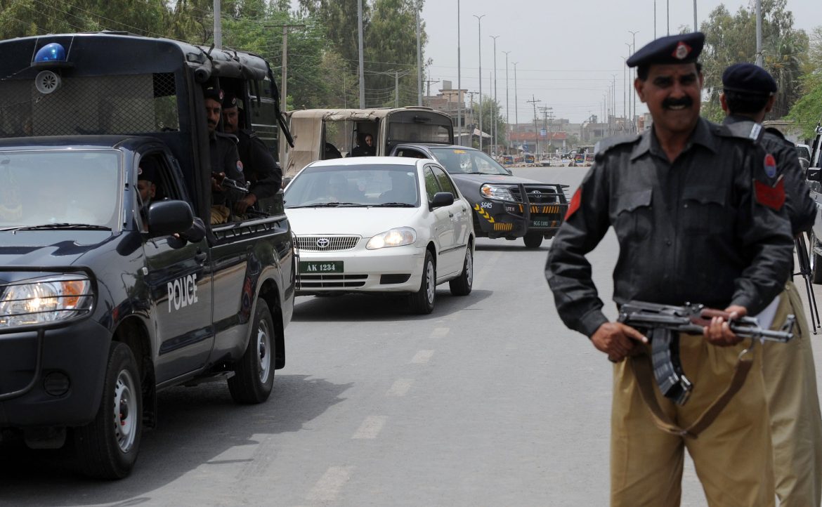 A police vehicle and armed officers monitor traffic on a busy street, ensuring security amid urban surroundings.