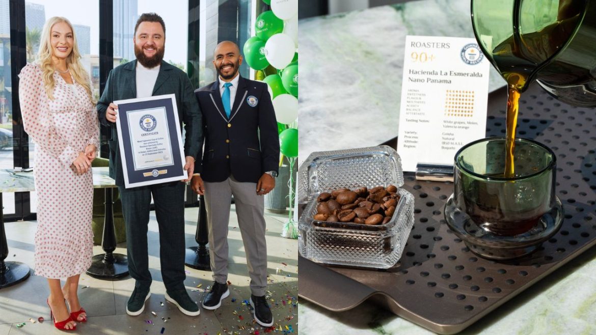 A rider in a green and white uniform guides a jumping horse over a wooden obstacle, flanked by red flags and lush greenery.