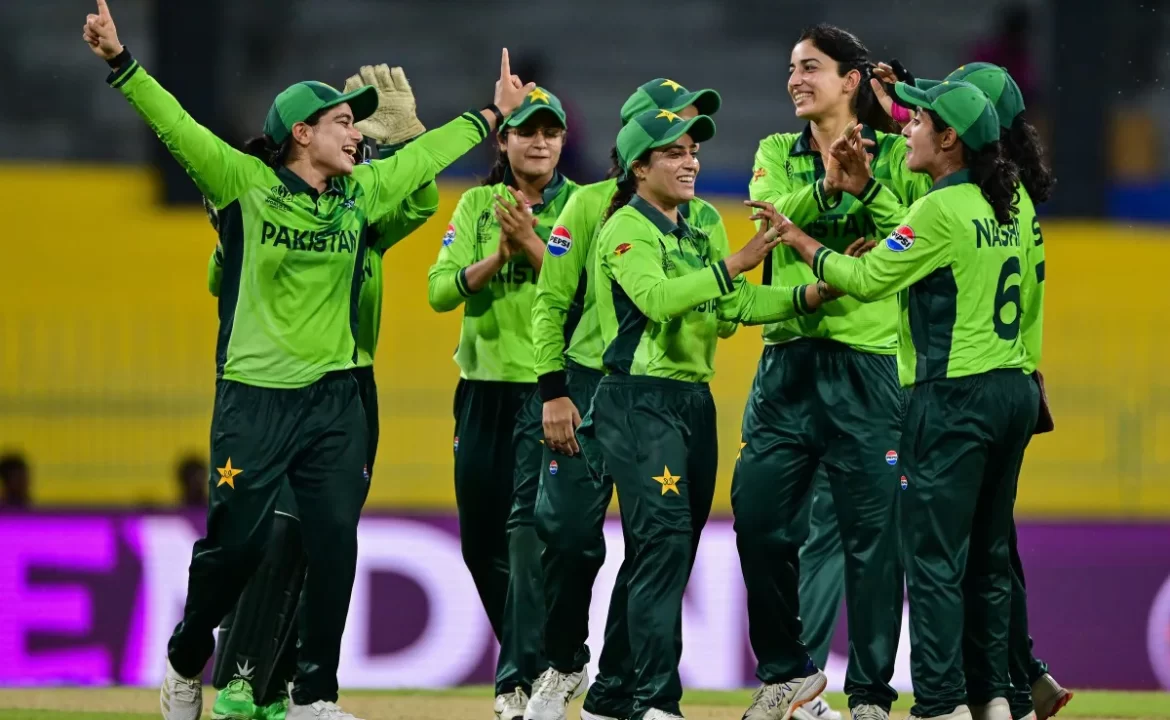 A group of jubilant Pakistani women cricketers celebrate a wicket, wearing green uniforms and displaying team spirit during a match.