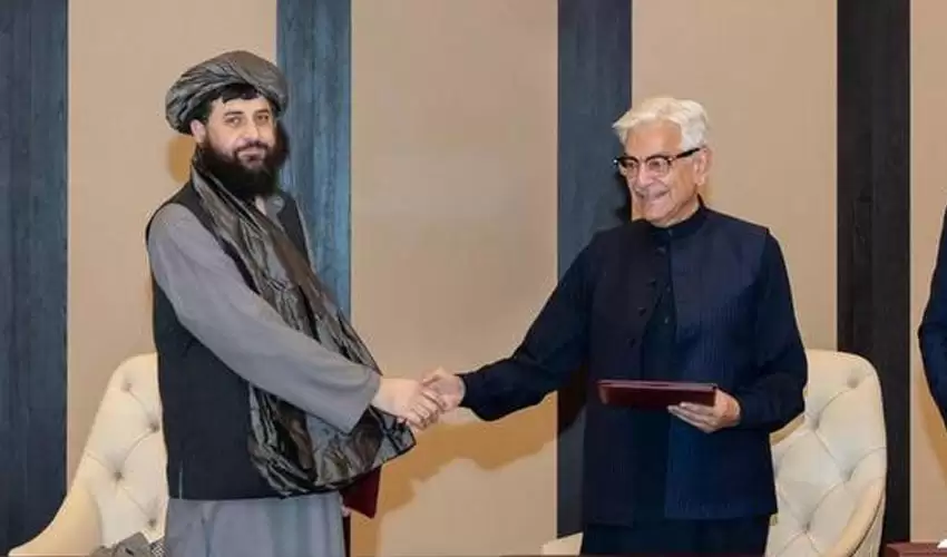 Two officials shake hands during a formal meeting, exchanging documents in a well-decorated setting.