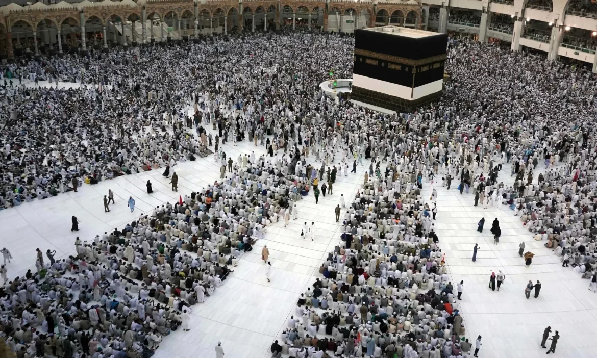Aerial view of thousands of pilgrims in white clothing surrounding the Kaaba at the Grand Mosque in Mecca during a religious gathering.