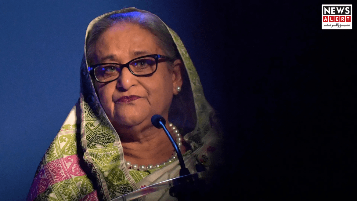 A woman in traditional attire speaks at a podium, illuminated by stage lights, with a dark background and a news alert graphic.