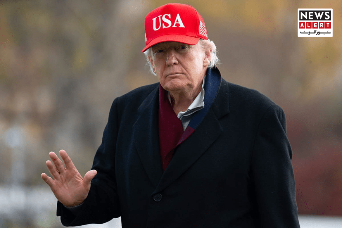 A man in a USA cap and dark coat raises his hand in a gesture, against a blurred autumn background. News alert banner in corner.