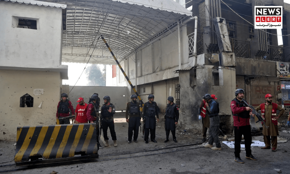 A group of armed police and rescue workers gather near a damaged building, with a barricade in the foreground and smoke in the air.