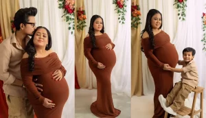 A pregnant woman in an elegant brown dress poses confidently, accompanied by a young boy and a partner, against a floral backdrop.