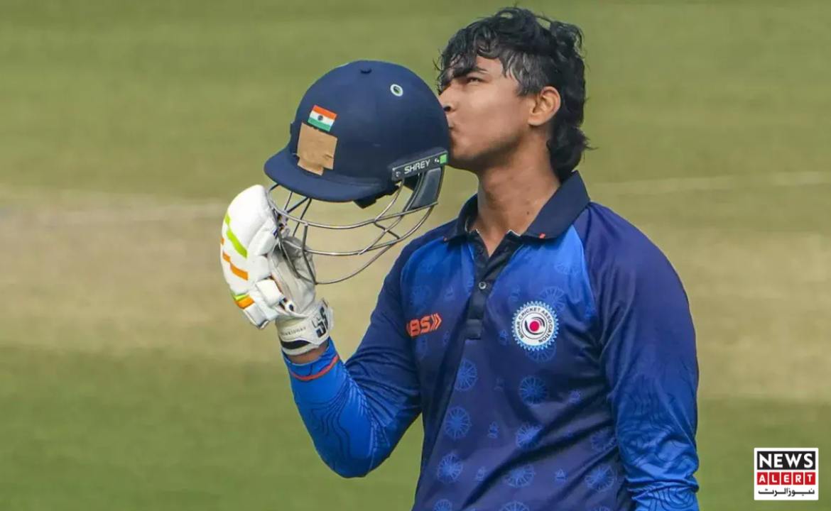 A cricket player in a blue jersey holds a helmet with an Indian flag sticker, standing on a cricket field.