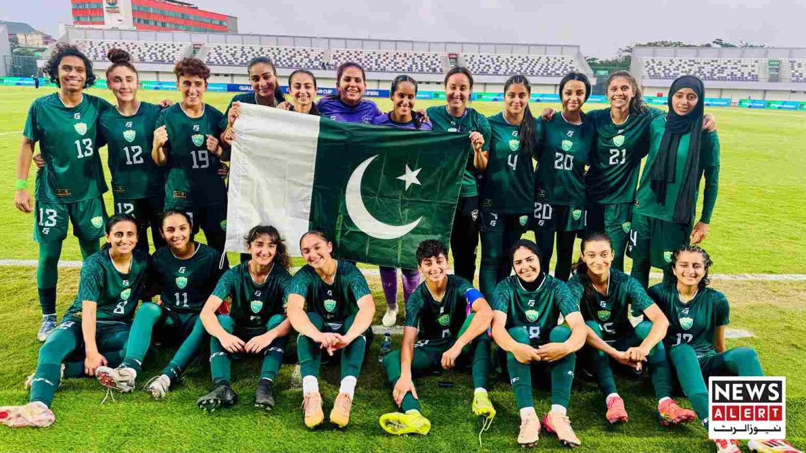 A group of soccer players in green uniforms hold a Pakistani flag while posing together on a sports field.