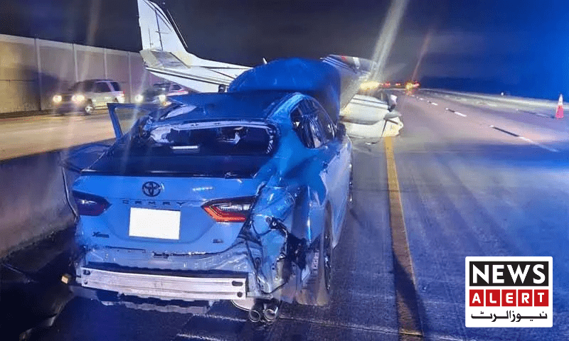 A damaged blue Toyota Camry is parked on a highway next to a small plane that has landed on the road, with police lights in the background.