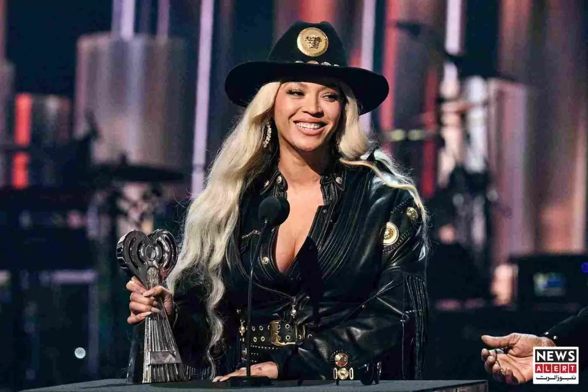 A person in a black leather outfit with silver accents holds an award at a podium, with a blurred background of a stage.