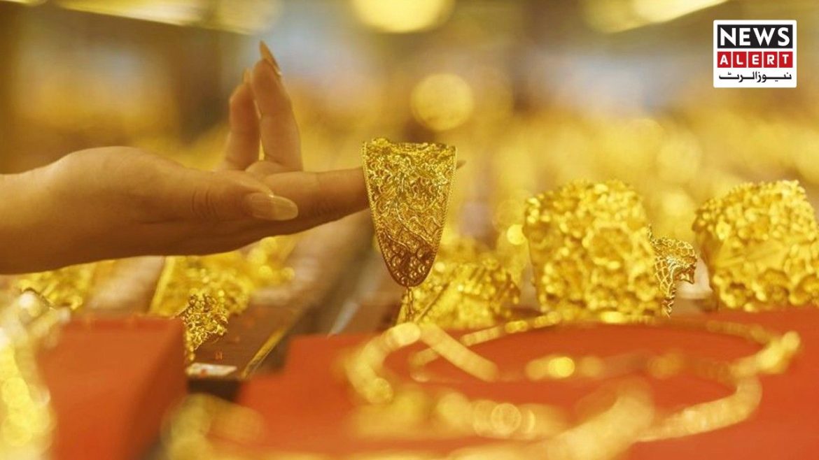 A person's hand reaches for an intricate gold bracelet among various gold jewelry on display in a brightly lit shop.