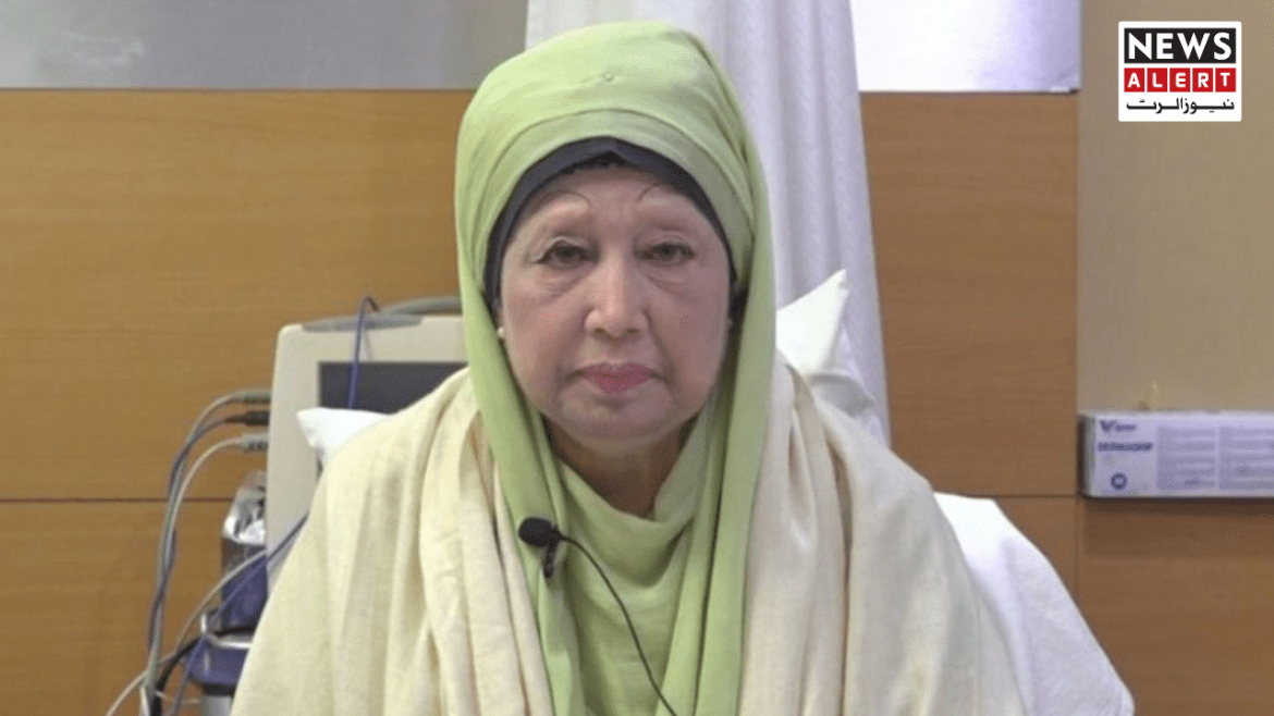 A woman in traditional attire with a green scarf sits on a hospital bed, surrounded by medical equipment and a neutral-colored background.