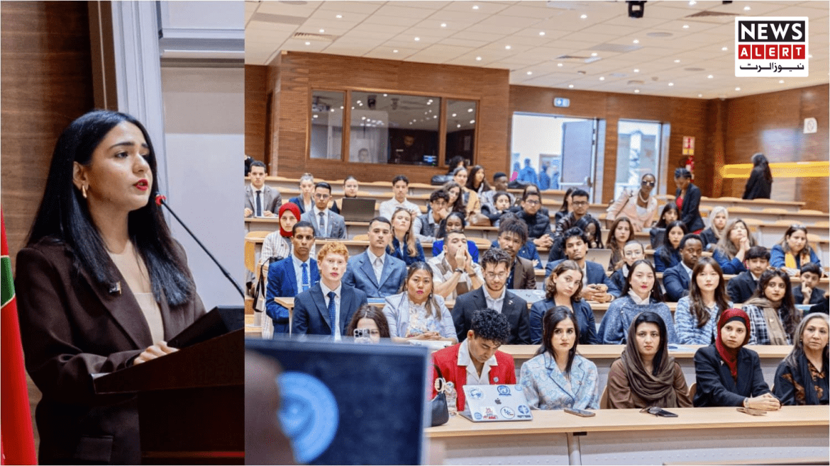 A speaker addresses a large audience in a modern lecture hall, with attendees attentively listening and engaged.