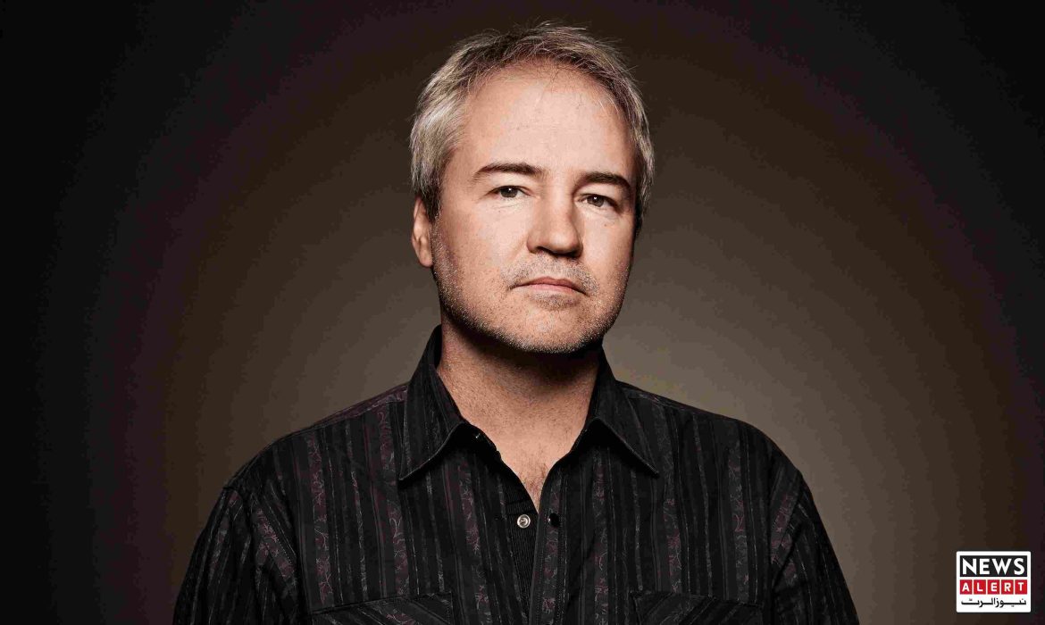 A person stands against a dark background, wearing a striped black shirt, with an abstract effect covering the face.