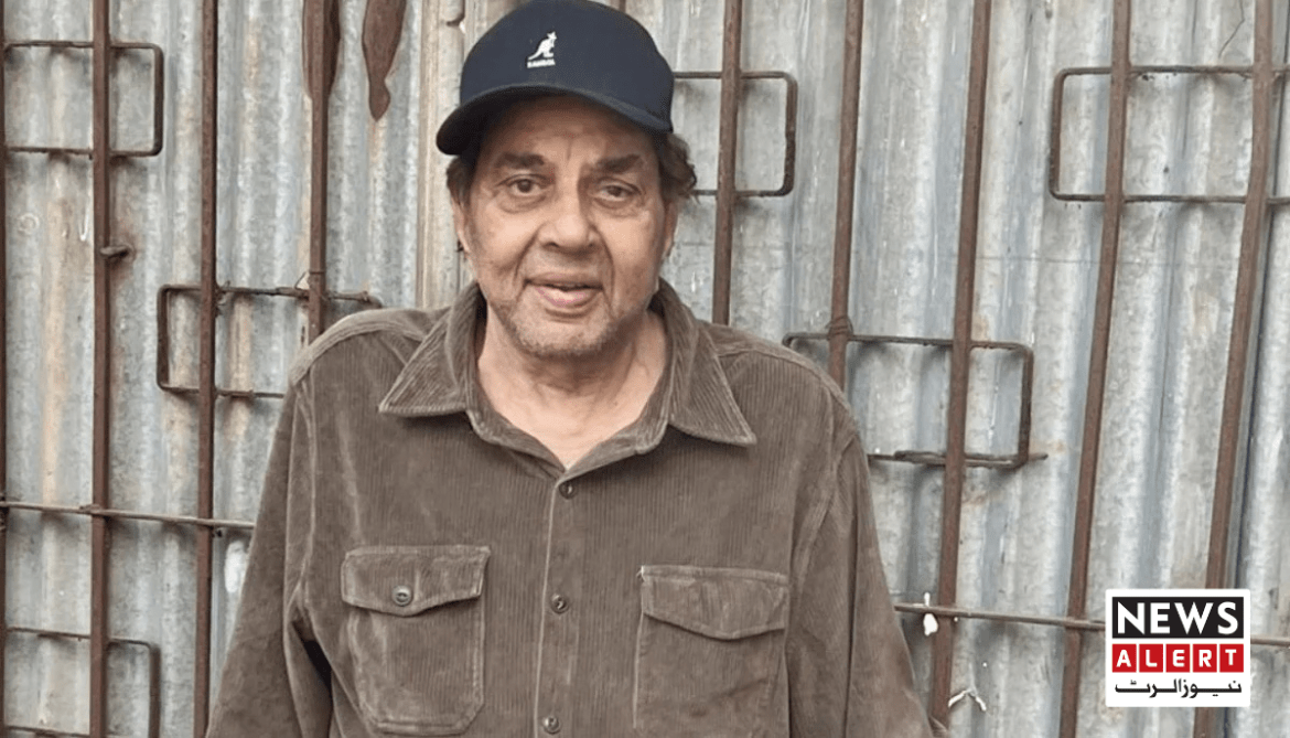 An older man stands in front of a corrugated metal wall wearing a dark jacket and a black cap, with industrial bars in the background.
