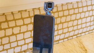 A sleek smartphone with a small, pivoting camera mounted on top, standing on a textured surface with a grid pattern in the background.